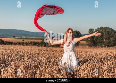 All'aperto foto di giovane, zenzero ragazza in abito bianco che tiene una sciarpa rossa che si accende in aria. Spazio di copia Foto Stock