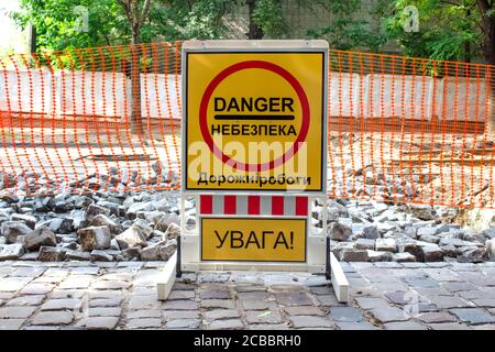 Strada interna con vecchio marciapiede, chiusa da blocchi stradali in pietra durante la ricostruzione. Cartello giallo con le parole in ucraino significa - PERICOLO, STRADA Foto Stock