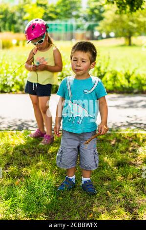 POZNAN, POLONIA - 26 luglio 2020: Piccolo ragazzo che tiene un albero torcente in piedi su erba verde in una giornata di sole in un parco Foto Stock