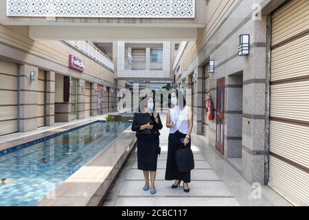 Due donne indiane che indossano maschere di protezione Covid-19 hanno una discussione in un ambiente urbano aziendale. Foto Stock