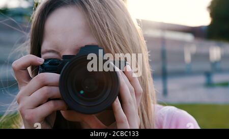 Foto all'aperto. Fotografo femminile che guarda attraverso il mirino della sua fotocamera dslr. Foto di alta qualità Foto Stock