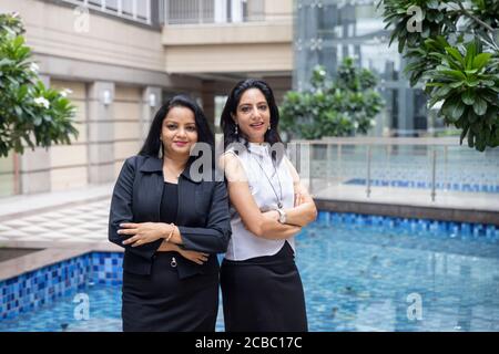 Due astute donne indiane che si levano fianco a fianco con le loro braccia incrociate in un ambiente urbano corporativo. Foto Stock