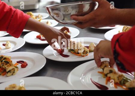 Colpo di closeup di mani cuochi che decorano piatti bianchi di arrostito e filetti di pollo affettati Foto Stock