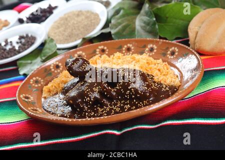 Pollo coperto in salsa alla talpa messicana, semi di sesamo accanto al riso cotto sul piatto Foto Stock