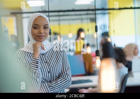 Donna di affari musulmana che indossa hijab e lavora al computer in ufficio. Bella donna africana in hijab guardando la macchina fotografica e sorridendo. Concetto di workplac Foto Stock