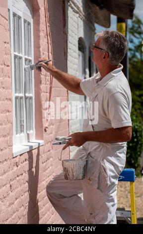 Hampshire, Inghilterra, Regno Unito. 2020. Pittore decoratore pittura piccole finestre su una casa rurale Foto Stock