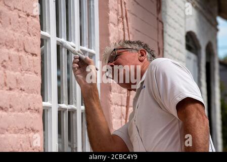 Hampshire, Inghilterra, Regno Unito. 2020. Pittore decoratore pittura piccole finestre su una casa rurale Foto Stock