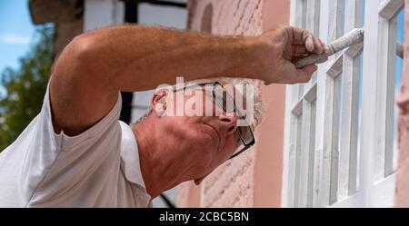 Hampshire, Inghilterra, Regno Unito. 2020. Pittore decoratore pittura piccole finestre su una casa rurale Foto Stock