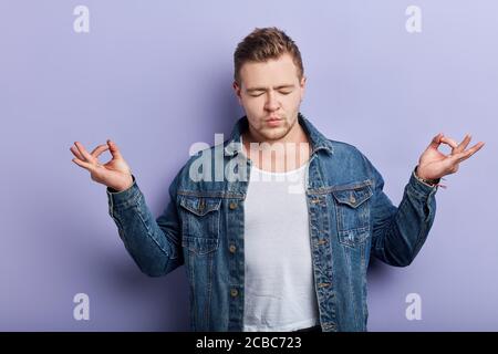 Giovane uomo forte e muscoloso che indossa una giacca in denim, si sente rilassato, facendo un gesto di meditazione con le dita. Yoga concept.neditazione, stile di vita, hobby Foto Stock