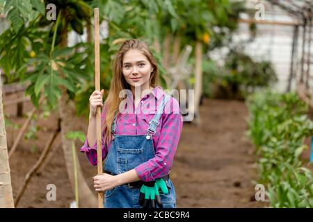 Donna che indossa jeans e camicia nel suo giardino in posa con una pala. Primo piano tiro. Copia spazio. Foto Stock