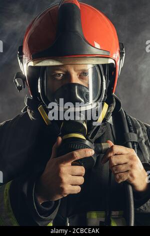 ritratto di vigile del fuoco sicuro in uniforme protettiva guardando la fotocamera, indossando un casco rosso Foto Stock