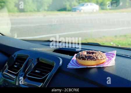 Ciambella per pranzo. Spuntino al cioccolato sulla console in auto. Pausa pranzo durante il viaggio in auto. Takeaway, social media. Foto Stock