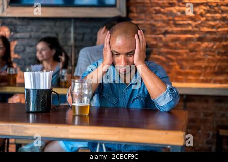 Un uomo latino triste e solitario seduto in un bar o in un pub mentre beve birra. Foto Stock