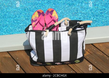 Borsa da spiaggia e accessori sul bordo di una piscina Foto Stock