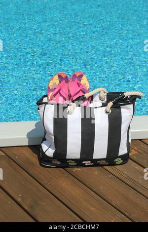 Borsa da spiaggia e accessori sul bordo di una piscina Foto Stock