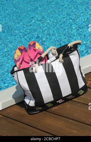 Borsa da spiaggia e accessori sul bordo di una piscina Foto Stock