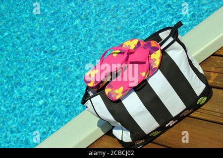 Borsa da spiaggia e accessori sul bordo di una piscina Foto Stock