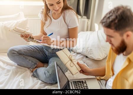 giovane coppia caucasica sposata lavoro al portatile e risolvere o preparare lettere a casa. bella coppia sedersi con lettere, inviti Foto Stock