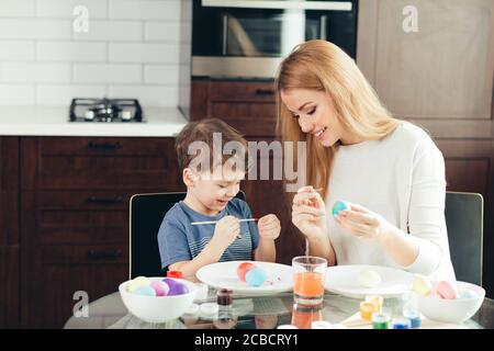 Felice famiglia amorevole della madre e del figlio la preparazione di decorazioni di Pasqua. La madre e il bambino ragazzo di copertura sono uova sode con vernici colorate e divertirsi Foto Stock