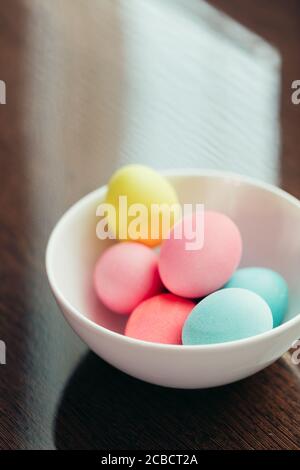 Uova di Pasqua con colori pastello poste in ciotola bianca sopra primo piano su sfondo scuro Foto Stock