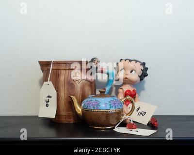 Bambola Betty Boop in legno d'epoca, caraffa collinosa e piccola teiera con i tag di prezzo alla vendita della proprietà su un tavolo nero. Foto Stock