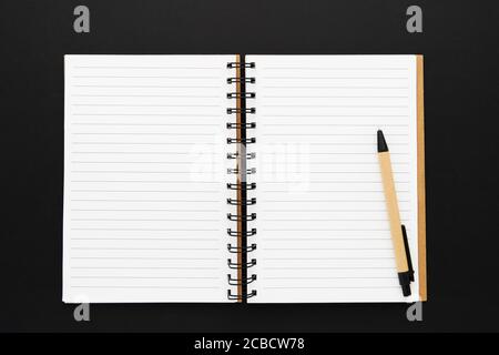 Il notebook di carta riciclata si è aperto su un foglio vuoto su sfondo nero. Copia spazio per testo, vista dall'alto. Foto Stock