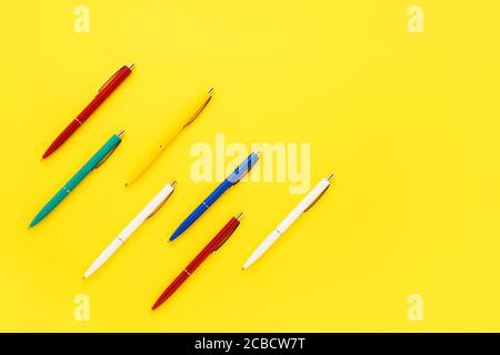Sette colorate penne a sfera su uno sfondo giallo brillante. Vista dall'alto, spazio di copia per il testo. Concetto di ritorno a scuola Foto Stock