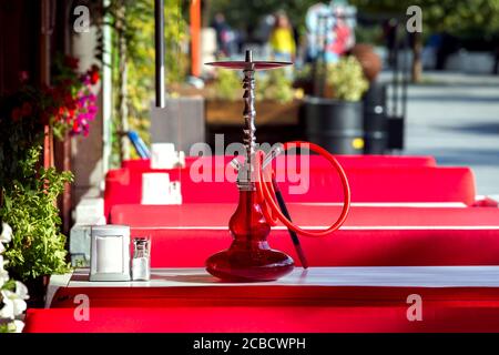 Terrazza estiva caffè all'aperto con tavoli bianchi e divani rossi, n il tavolo è un gancio di vetro rosso con un tubo per fumare, nessuno. Foto Stock