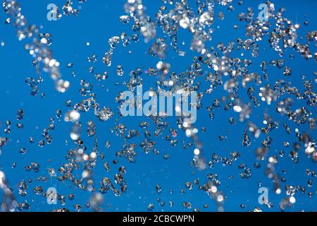 Spruzzi d'acqua contro il cielo blu, spruzzi rinfrescanti liquidi su uno sfondo blu. Foto Stock