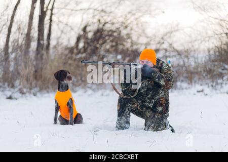 giovane uomo in camouflage guardando un animale. foto a lunghezza intera. stagione di caccia Foto Stock