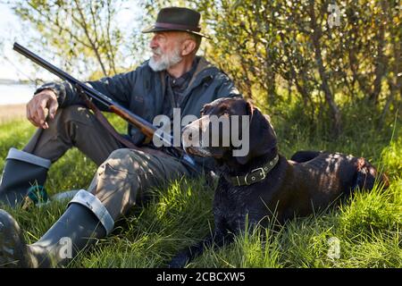 Ricerca trofeo con cane. Uomo anziano pronto a cacciare. Siediti riposando prima di andare a caccia Foto Stock