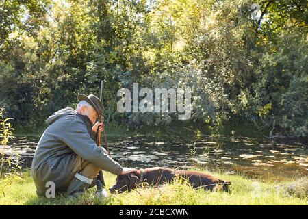 Riposarsi prima di andare a caccia. Hunter uomo sul lago, tenendo fucile Foto Stock