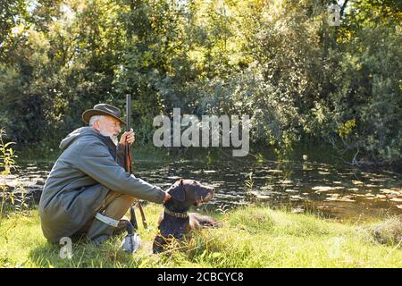 Riposarsi prima di andare a caccia. Hunter uomo sul lago, tenendo fucile Foto Stock