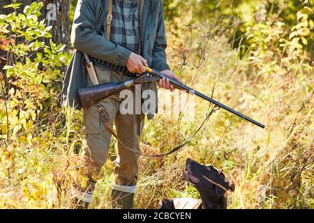 Nero aiutante labrador con il suo proprietario cacciatore uomo in foresta. Fucile a caricamento maschio Foto Stock