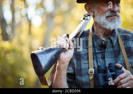 Uomo cacciatore con bearded con pistola sulla spalla, binoculare in una mano. Cercare trofeo in foresta Foto Stock