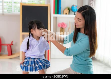 Madre asiatica intreccio i suoi capelli delle figlie seduti sulla sedia, sorriing sorella singola mamma aiutare la ragazza del bambino con acconciatura a casa ottenendo pronto a scuola Foto Stock