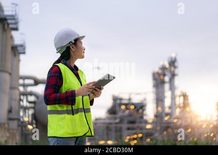 Donna asiatica ingegnere petrolchimico che lavora con tablet digitale all'interno di impianti di raffineria di petrolio e gas fabbrica per il controllo di qualità di sicurezza ispettore Foto Stock