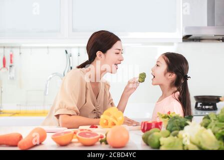 Felice madre e figlia bambino che preparano e mangiano le verdure e frutta Foto Stock