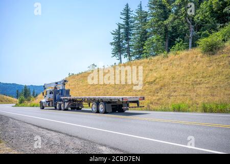 Semirimorchio bianco grande con applicazione di gru sul telaio per il trasporto di semirimorchi vuoti in marcia su strada tortuosa Con le colline a Columbia Go Foto Stock