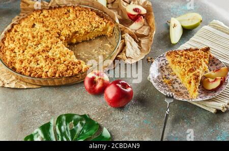 Torte fatte in casa, torta in un piatto da forno e una fetta su un piatto con pesche e pere su cemento grigio-blu. Foto Stock