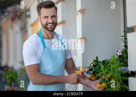 Giovane uomo bearded in piedi fuori negozio di fiori, spruzzando fiori Foto Stock