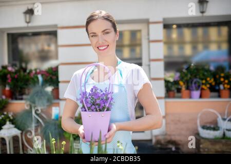 Affascinante femmina dai capelli scuri con labbra rosse che tengono in mano il fiore viola pentola fuori negozio di fiori Foto Stock