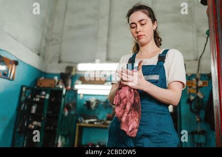 Uguaglianza di genere. Ritratto di una giovane donna forte in uniforme, che lavora in un laboratorio, che gli asciuga le mani con uno straccio. Bottom view.Auto Shop nel ba Foto Stock