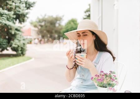 Estate. Bella giovane donna seduta in un caffè di strada e gusti gelato. Spazio di copia. Foto Stock