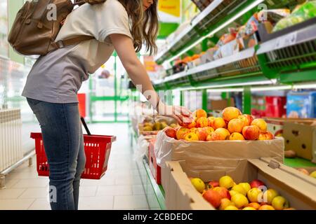 Ritratto di una giovane donna carina con un cesto in mano, che sceglie le mele nel supermercato. Foto Stock