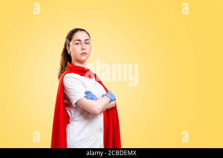 Un medico o un infermiere in guanti medici e un capo supereroe rosso su uno sfondo giallo. Spazio di copia. Super Hero potere per clinica e ospedale, assistenza sanitaria Foto Stock
