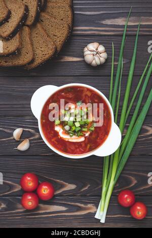 Zuppa di pomodoro fatta in casa con pane di segala e aglio su un tavolo di legno scuro. Zuppa di barbabietole in un recipiente con panna acida e cipolle verdi. Russo tradizionale c Foto Stock