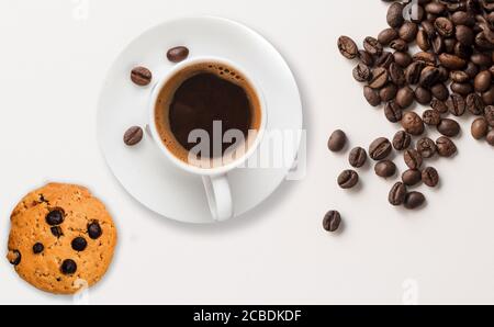 Chicchi di caffè marroni arrostiti, biscotti al cioccolato e una tazza di caffè su uno sfondo bianco. Foto Stock