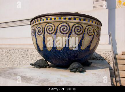 Una vista ravvicinata e dettagliata delle tartarughe di supporto in bronzo sotto la piantatrice, vaso di tegola a mosaico davanti all'ingresso a gradini della Secessione mu Foto Stock