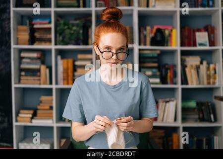 Bella gioiosa giovane donna rossa che indossa occhiali casual è lavorato a maglia vestiti fatti a mano con raggi. Foto Stock